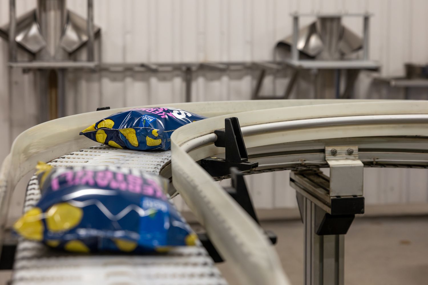 Colorful snack packages moving along curved conveyor belt in food manufacturing facility.