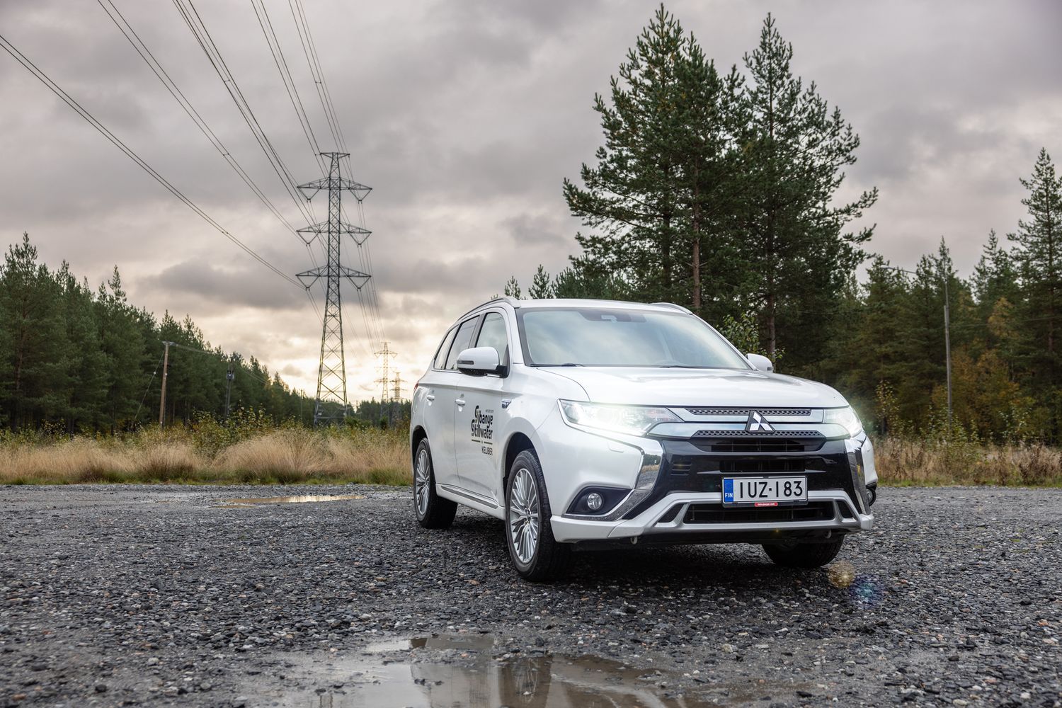 Valkoinen auto lähikuvassa, taustalla sähkölinjoja.