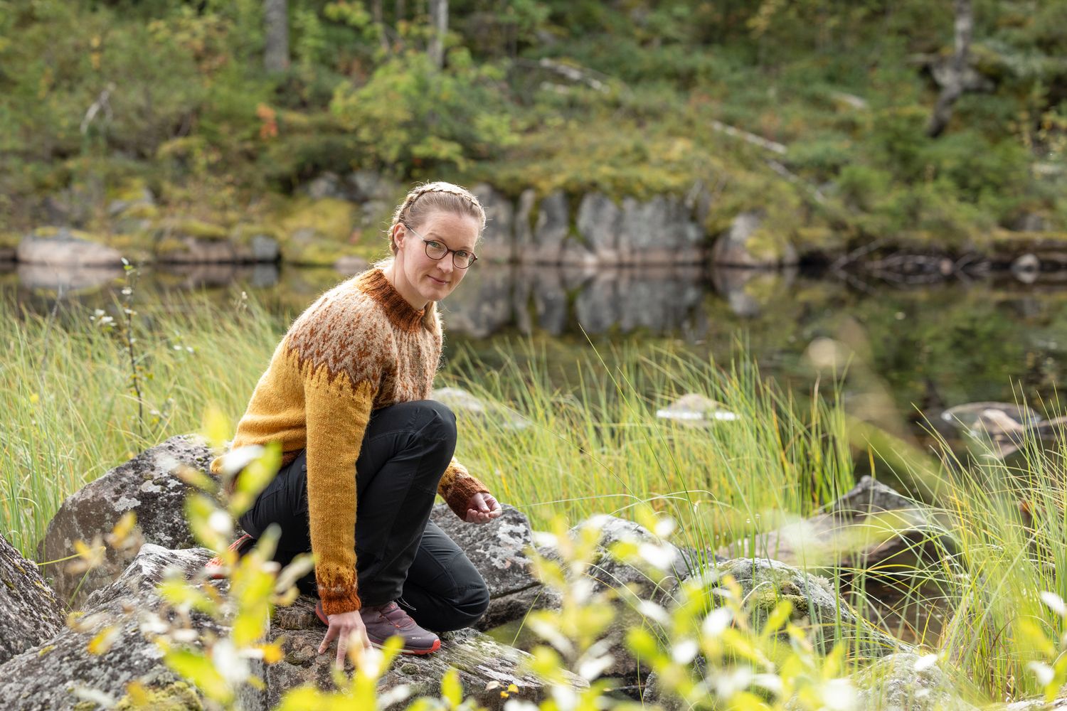 Neulepuseroon pukeutunut nainen istuu kyykyssä rantakivillä.