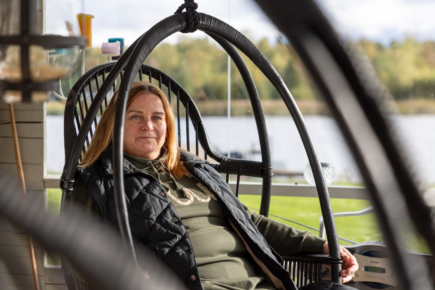 Nainen istuu ulkona terassilla mustassa, rottinkisessa keinussa.