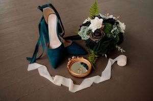 Wedding accessories including a teal dress, delicate greenery, and white floral arrangements displayed elegantly.
