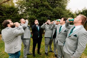 Groomsmen in grey suits taking celebratory drinks together outdoors.