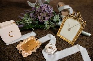 Wedding details flatlay with vintage frames, flowers and ribbons on dark wood surface.