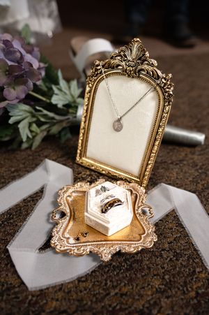 Ornate gold vintage frame with wedding details and jewelry arranged on brown textured background.