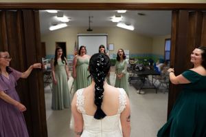 Bride getting confetti showered by bridesmaids in purple and green dresses.