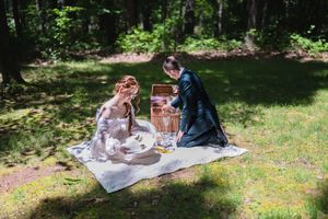 A couple enjoys a relaxing picnic on a blanket under shady trees in a tranquil park setting.