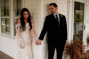 Wedding couple poses in formal attire on a white porch with rustic details and fall decor.
