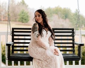 Someone in a flowy lace dress sits on a black porch swing in an outdoor setting.