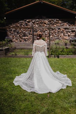 A bride in a stunning lace wedding gown standing in front of a rustic wood shed.
