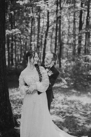 A couple shares an intimate dance moment in a sunlit forest setting wearing formal wedding attire.