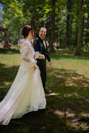 Candid wedding moments captured in a sunlit forest with flowing white dress.