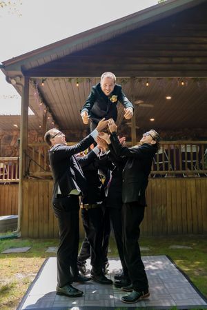 Groomsmen in black suits performing funny poses on a wooden deck.