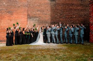 Large wedding party group photo lined up against a rustic brick wall outdoors.