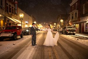 Snowy nighttime street scene with glowing lampposts and parked cars.