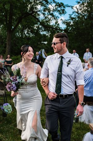 Wedding couple walks together on green lawn during outdoor celebration.