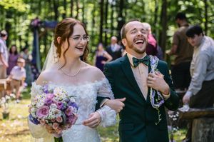Joyful wedding couple sharing a laugh together in a sunlit forest setting.