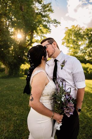 Wedding couple shares romantic sunset moment with purple floral bouquet.