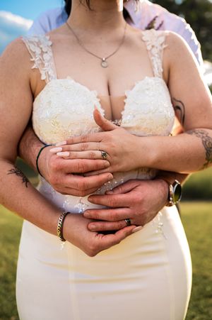 Close-up details of lace wedding dress and hands with rings.