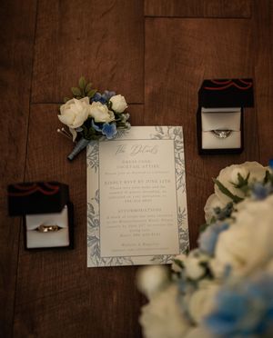 Wedding invitation and decorative elements arranged on dark wooden surface with blue and white flowers.