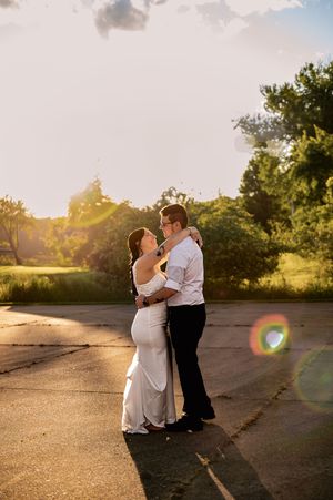 A couple in wedding attire shares an intimate moment at golden hour on a paved pathway.