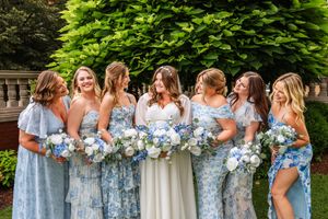 Bridesmaids in light blue floral dresses holding bouquets pose together outdoors.