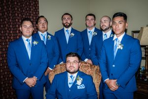 A wedding party in matching royal blue suits and light blue ties pose together with a seated member in the center.