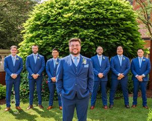 Groomsmen in matching royal blue suits stand in line against green garden backdrop.