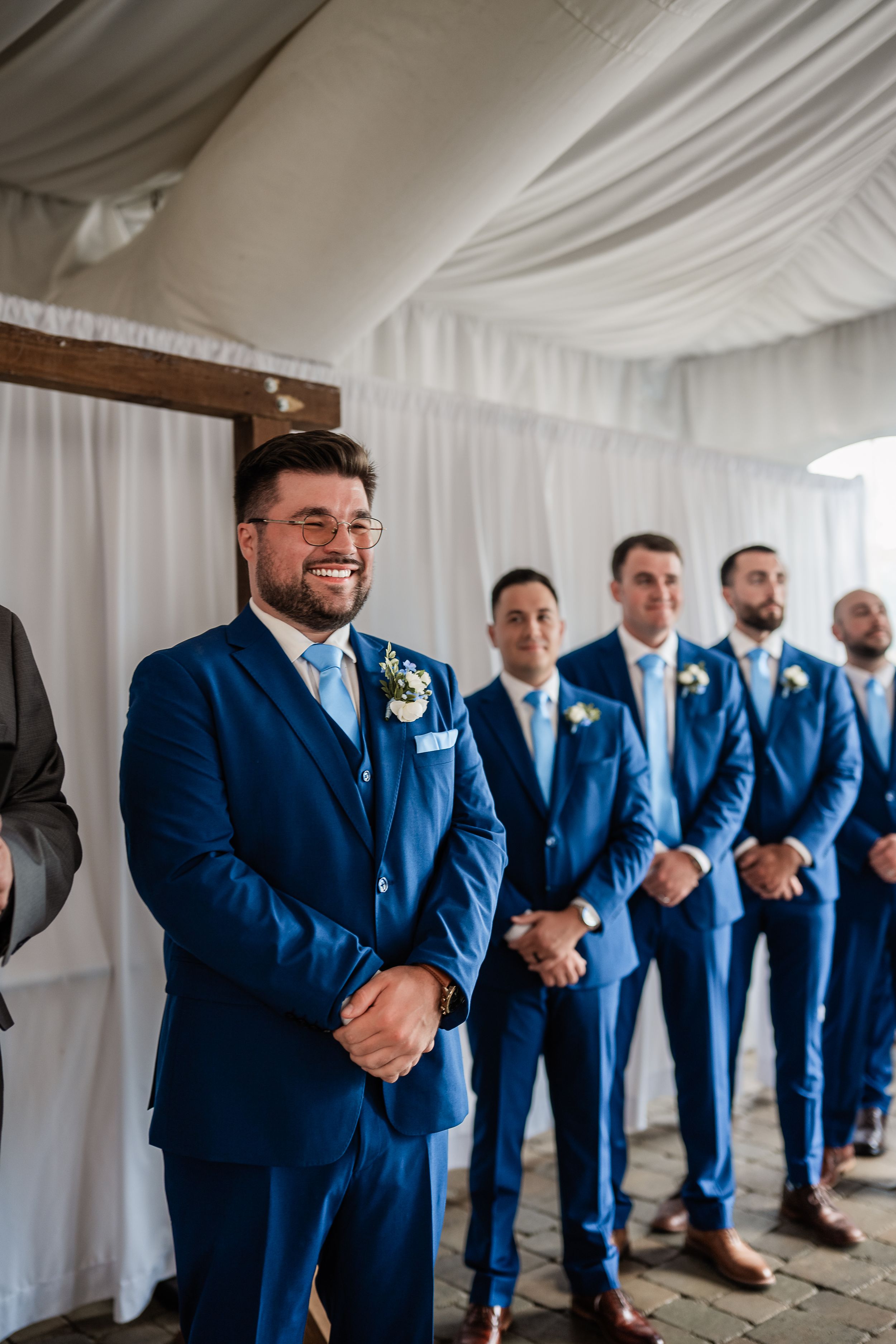 Groomsmen in coordinated navy blue suits posing together in a white tent venue.