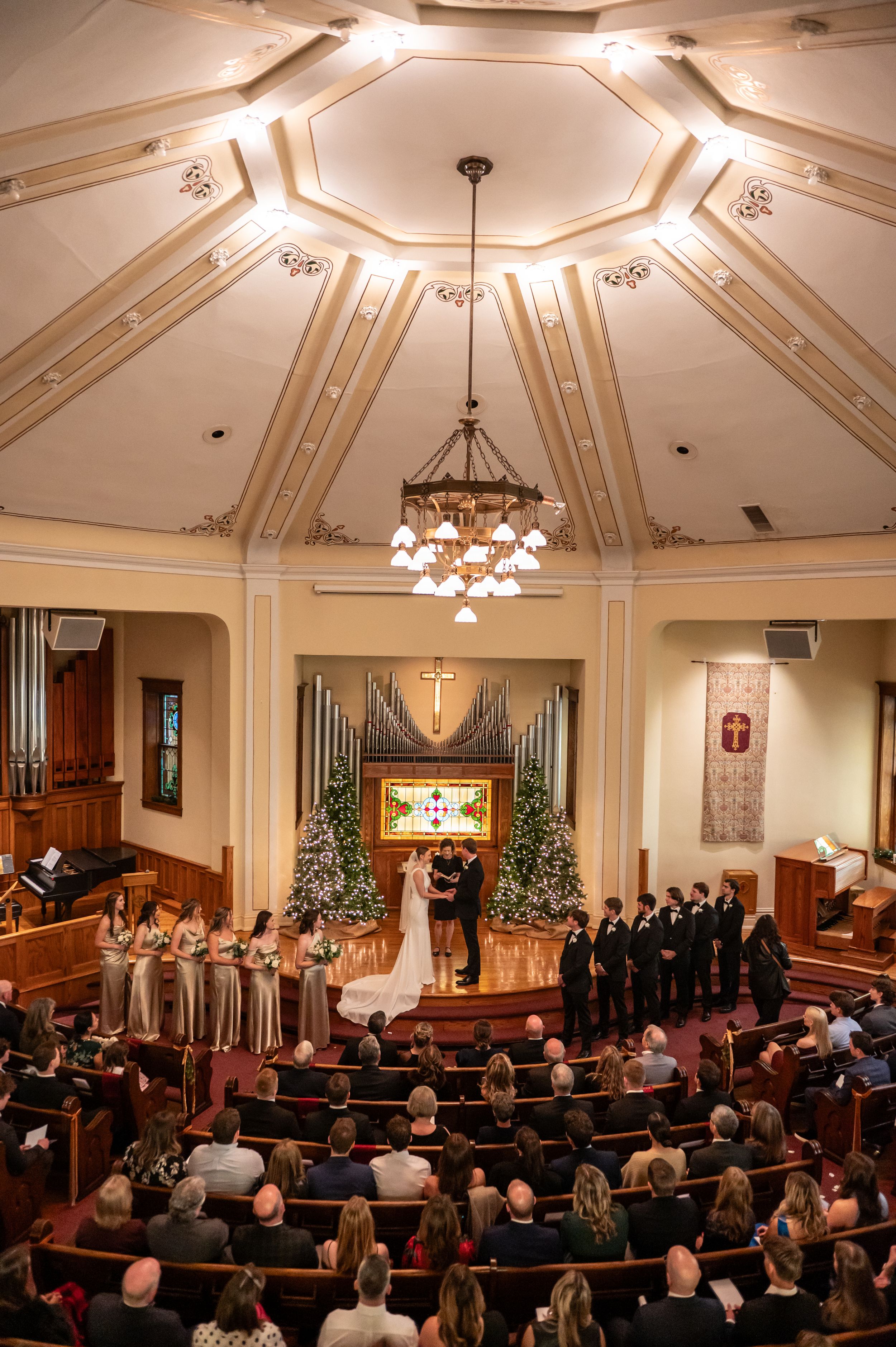 Ornate church ceiling and chandelier above wedding ceremony with decorated altar.