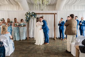 Wedding ceremony moments in white draped venue with blue and white decor details.