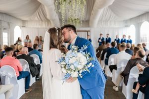 A wedding ceremony moment in a white tent with blue floral bouquet and elegant decor.