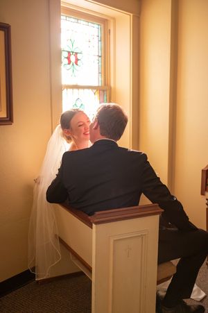 Bride and groom sitting together in a sunlit church alcove.