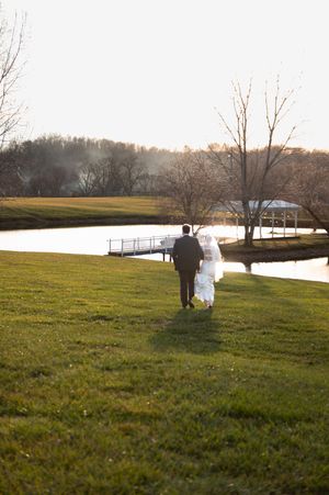 Couple walking through a scenic field at sunset near a lake.