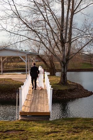 Wedding couple walking on a wooden bridge over calm waters.