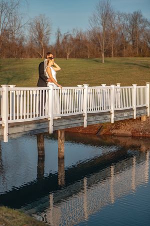 Couple crossing a white-railed bridge over reflective water.