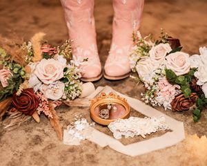 Close-up of delicate pink floral arrangements with wedding rings and decorative lace details.