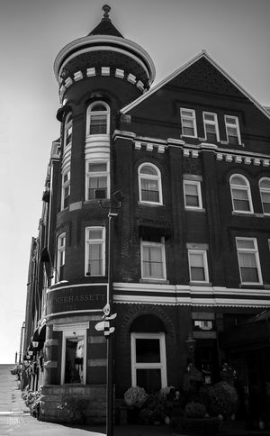 Historic brick building with Victorian architectural features shown in black and white with distinctive turret and windows.