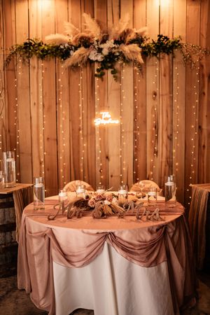 Elegant wedding reception setup with string lights and draped tables in rustic wooden barn venue.