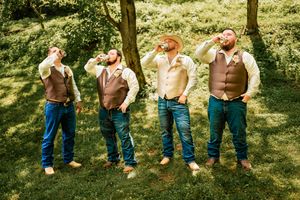 Groomsmen in jeans showing off their boots in a creative outdoor wedding photo.