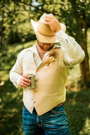 Close-up of western style groomsman adjusting tan vest in outdoor setting.