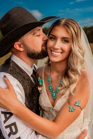 A western-style wedding photo features turquoise jewelry accents and a black cowboy hat against a bright blue sky.