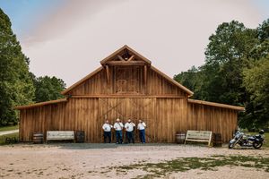 Panoramic view of a rustic wooden barn venue surrounded by trees and open fields.