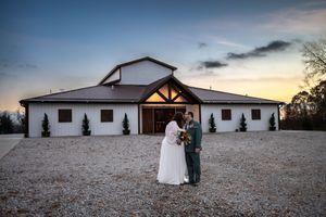 A wedding venue exterior with white walls and wooden beams is shown at sunset against a dramatic sky.