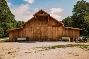 Wide angle view of a wooden barn event venue with gravel parking area and natural landscape.