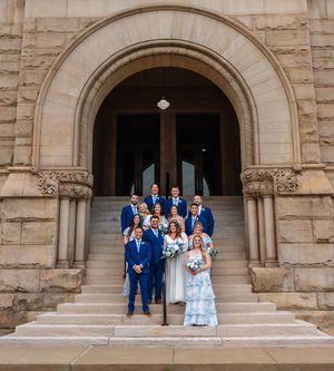 Wedding party posing on stone steps of an ornate historic building with arched doorways.