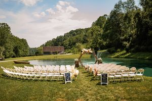 Outdoor wedding ceremony setup with white chairs arranged on a sunny green hillside.
