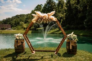 Wedding ceremony arch decorated with flowers stands near a lake with fountains creating a romantic outdoor setting.