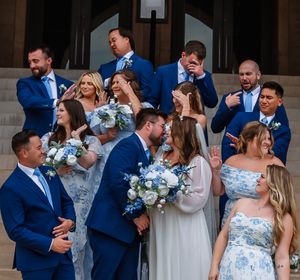 Wedding party in navy suits and light dresses posed in coordinated lineup outdoors.