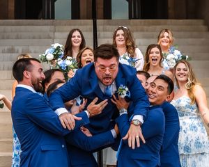 Groomsmen sharing celebratory group hugs in blue suits outdoors.