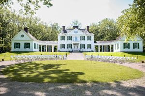 An elegant white colonial mansion set up for an outdoor wedding ceremony with rows of white chairs.